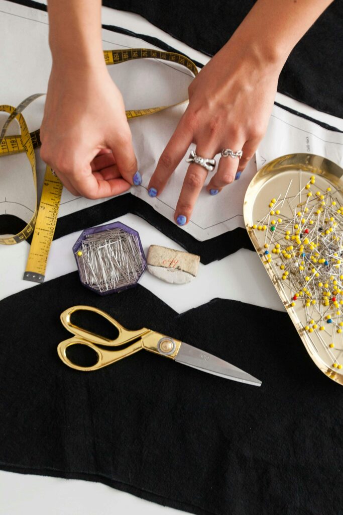 Close-up of a tailor's workspace with hands pinning fabric, measuring tape, scissors, and pins.